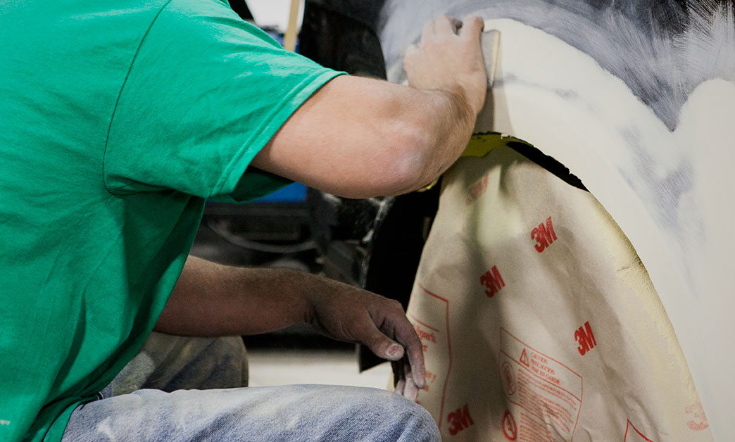 | Schaefer Autobody Centers person bending down and sanding damage on vehicle
