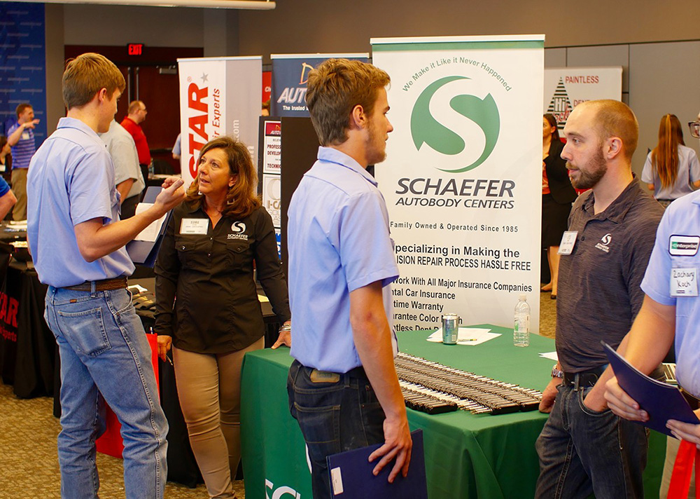 | Schaefer Autobody Centers schaefer employees standing and talking around a table at career fair