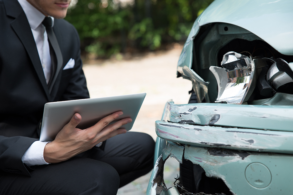 Side view of writing on clipboard while insurance agent examining car after accident