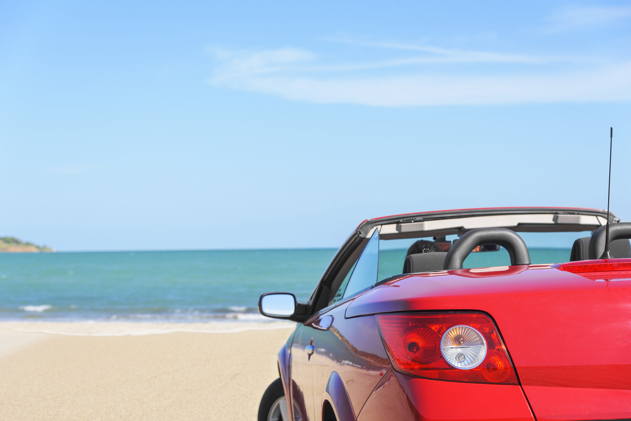 red parked car sitting on beach facing the ocen