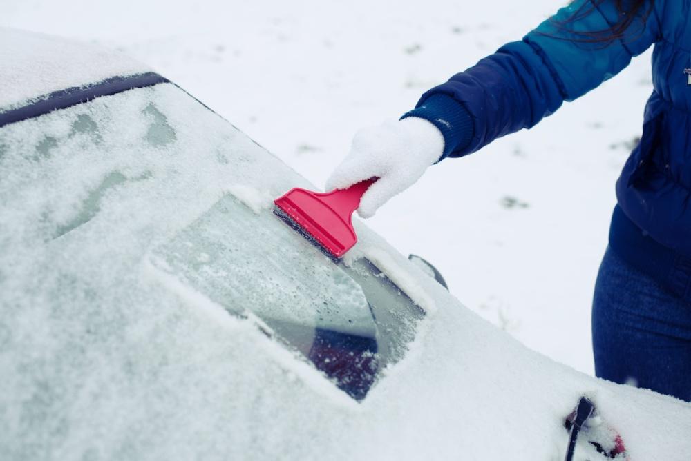 person scraping snow and ice from their car's windshield