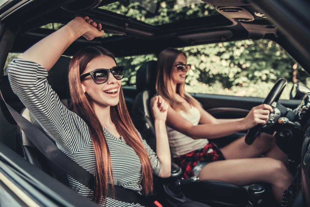 girls in sun glasses are smiling while traveling by car
