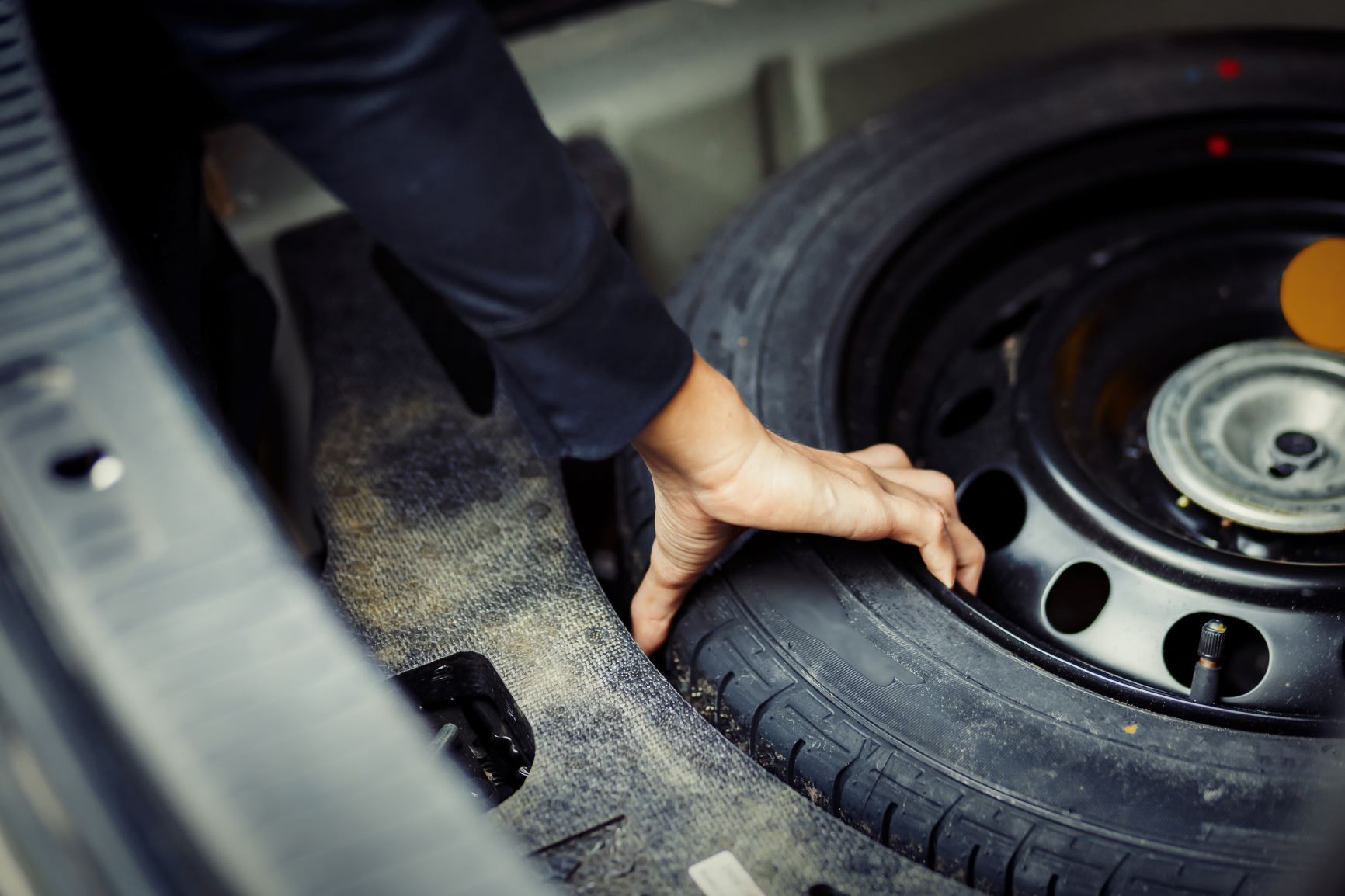 person grabs spare tire out of trunk of car