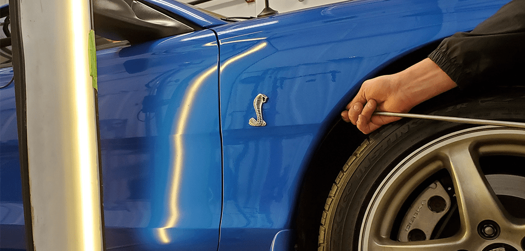 Hand reaching into frame to remove dent from a blue sports car