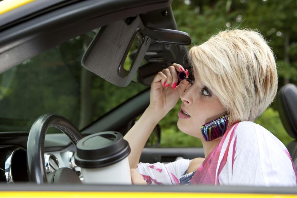AdobeStock_30341149 | Schaefer Autobody Centers woman driving car while applying mascara, talking on her phone, and holding a coffee