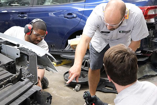 Journeyman instructs an apprentice on repairs to a car