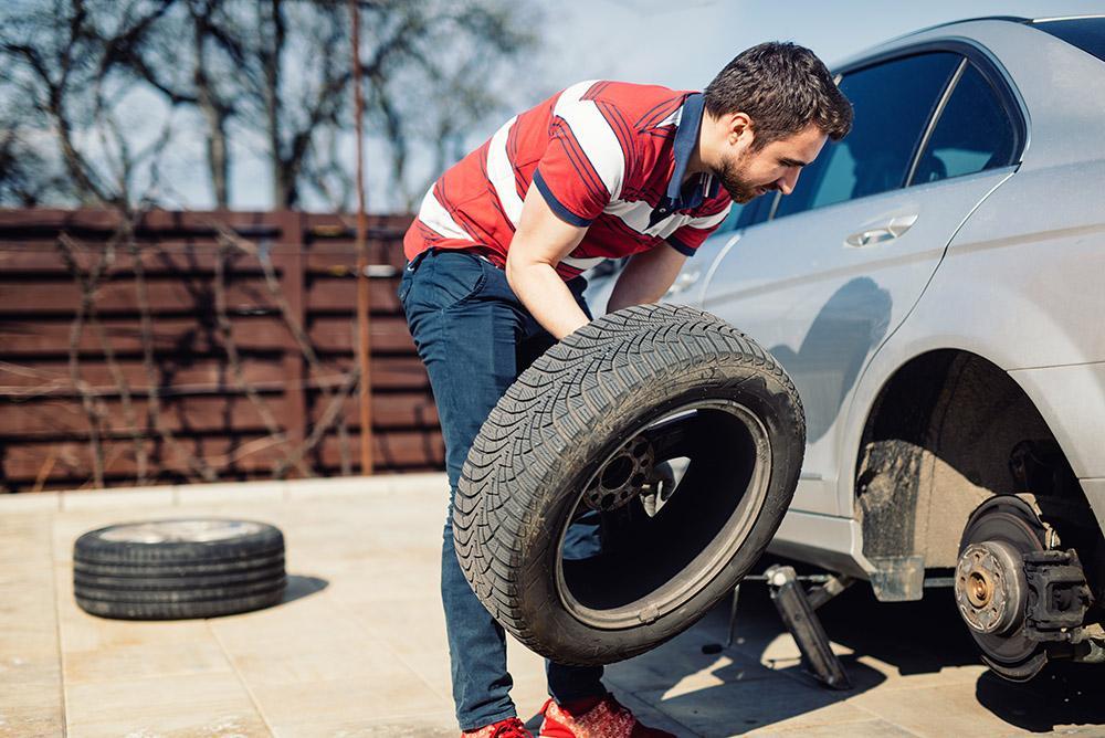 Changing a flat car tire in the backyard. Tire maintenance, dama | Schaefer Autobody Centers man is changing a flat tire