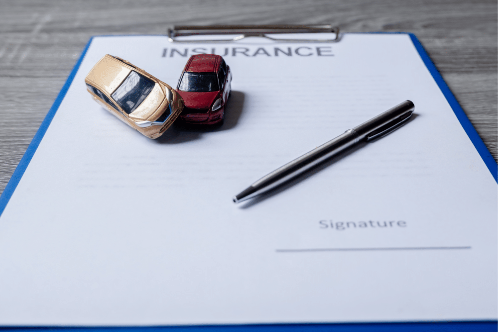insurance paper with a pen and two toy cars in an accident