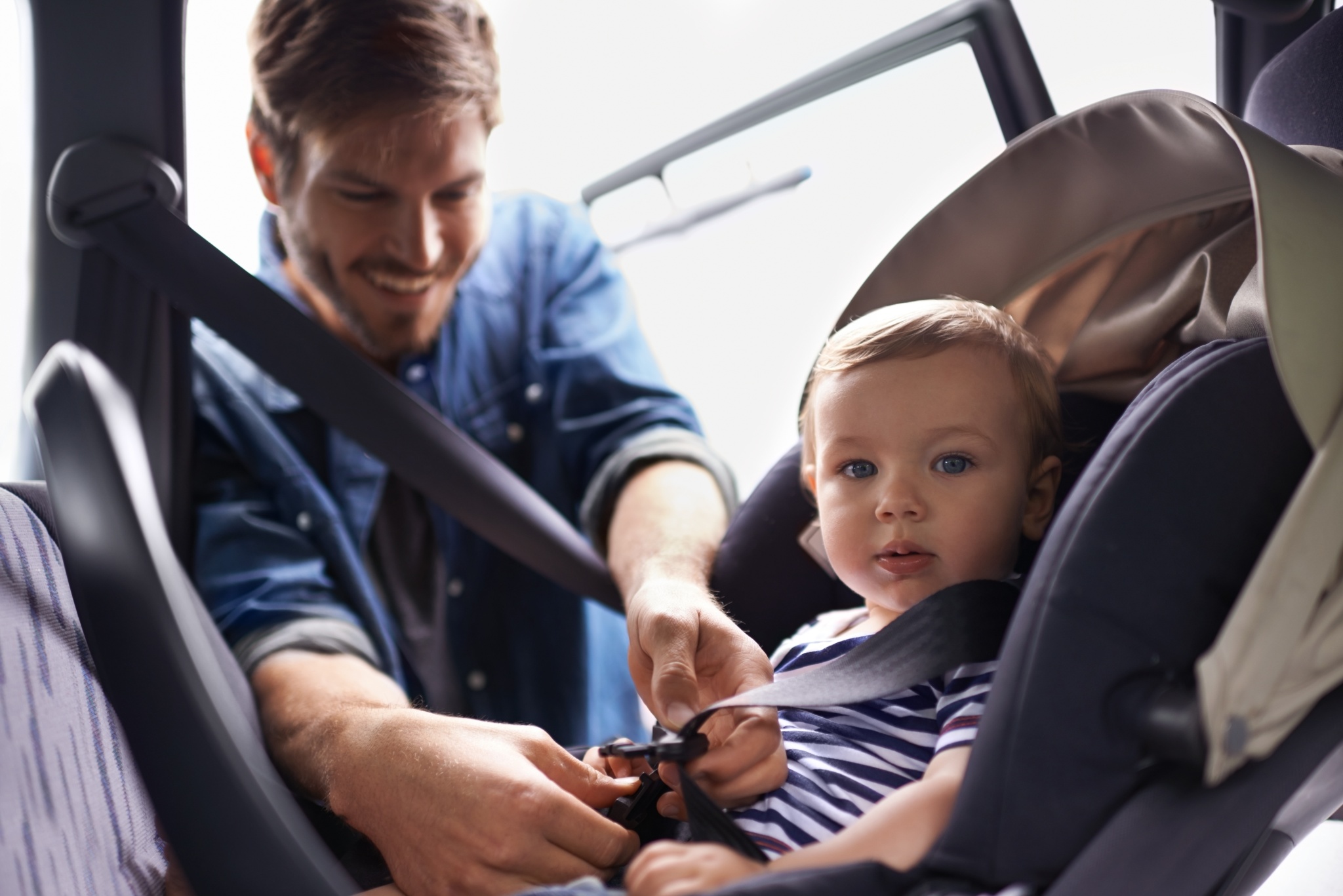 A young father strapping his baby into a car seat.
