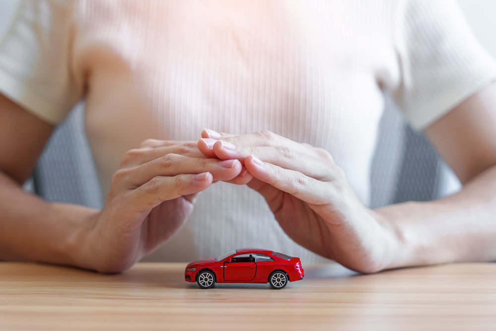 hand-cover-or-protection-red-car-toy-on-table | Schaefer Autobody Centers Hands covering a small replica car